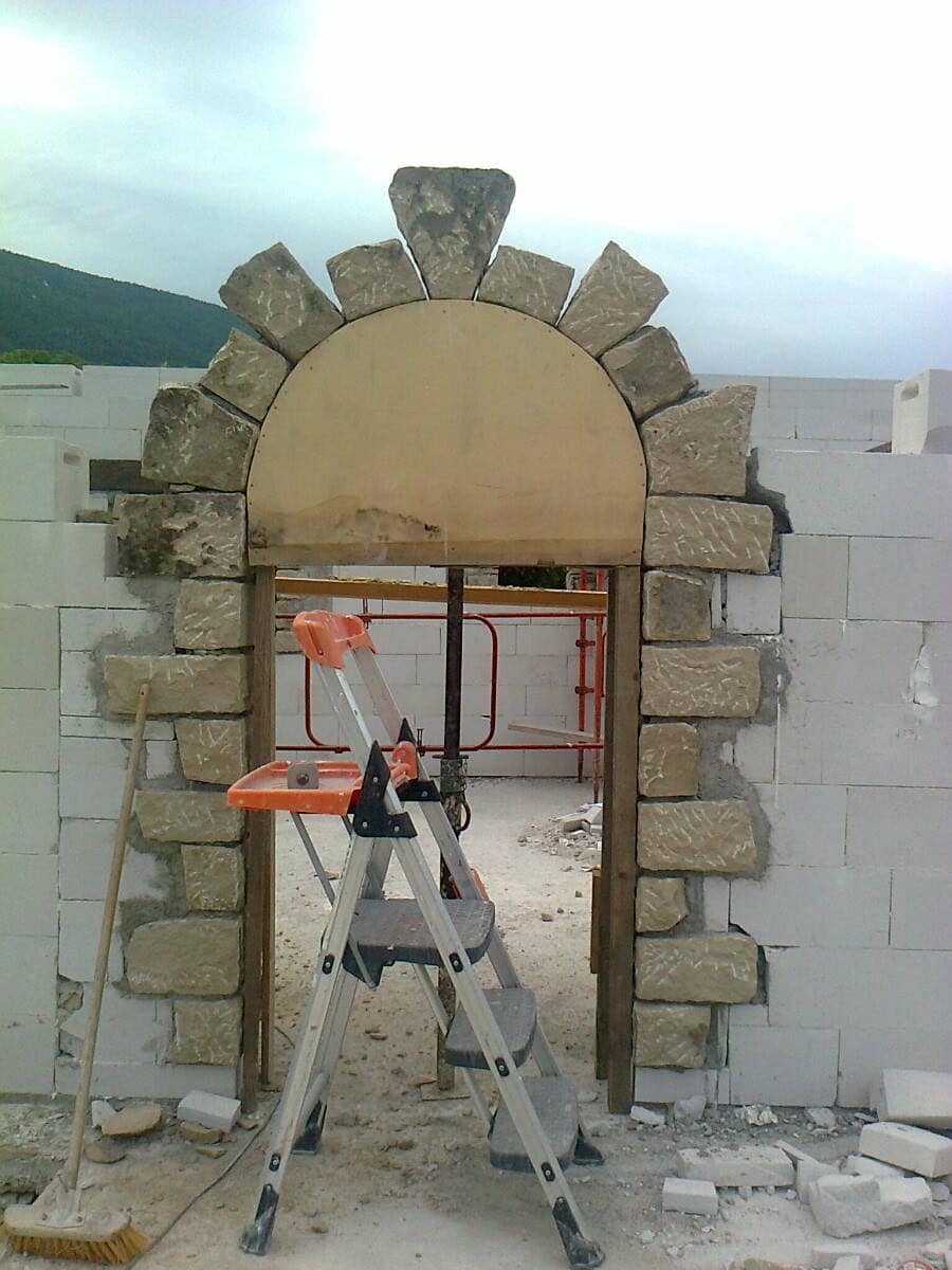 Arc en pierre monté sur son cintre de bois, dans un mur en cours d'élévation.