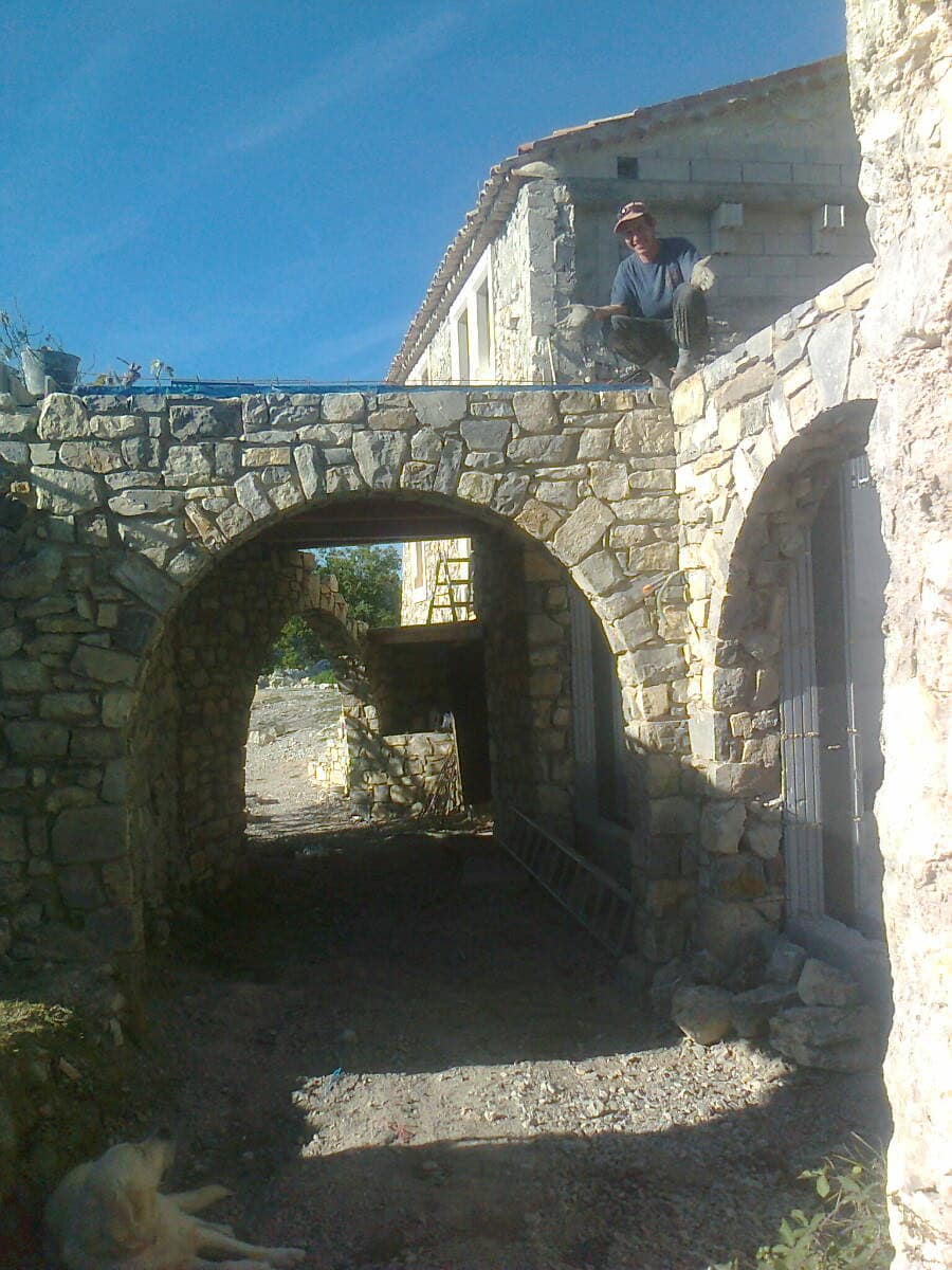 Passage voûté monté en pierre, deux arcs en enfilade, maçon assis sur le mur en construction.