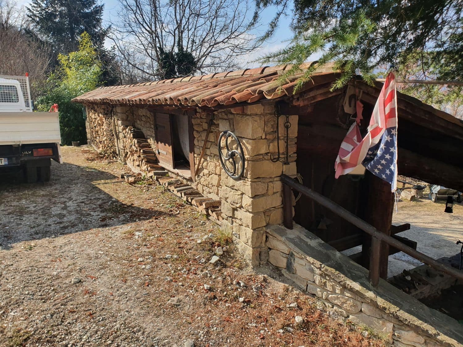 Longue bâtisse basse en pierre, toiture en tuiles anciennes et appentis de bois.