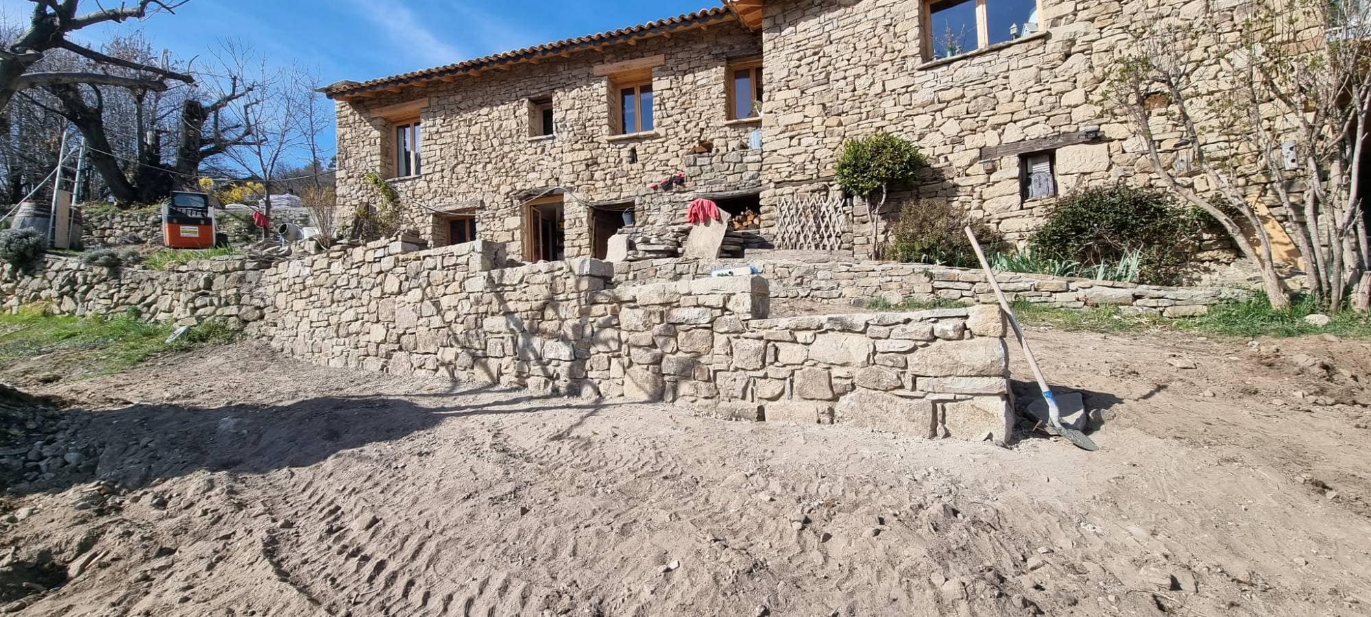 Bâtisse en pierre d'un hameau de Braux : murs de soutènement et escalier en pierre sèche montés devant la maison, terrain en cours de reprise.