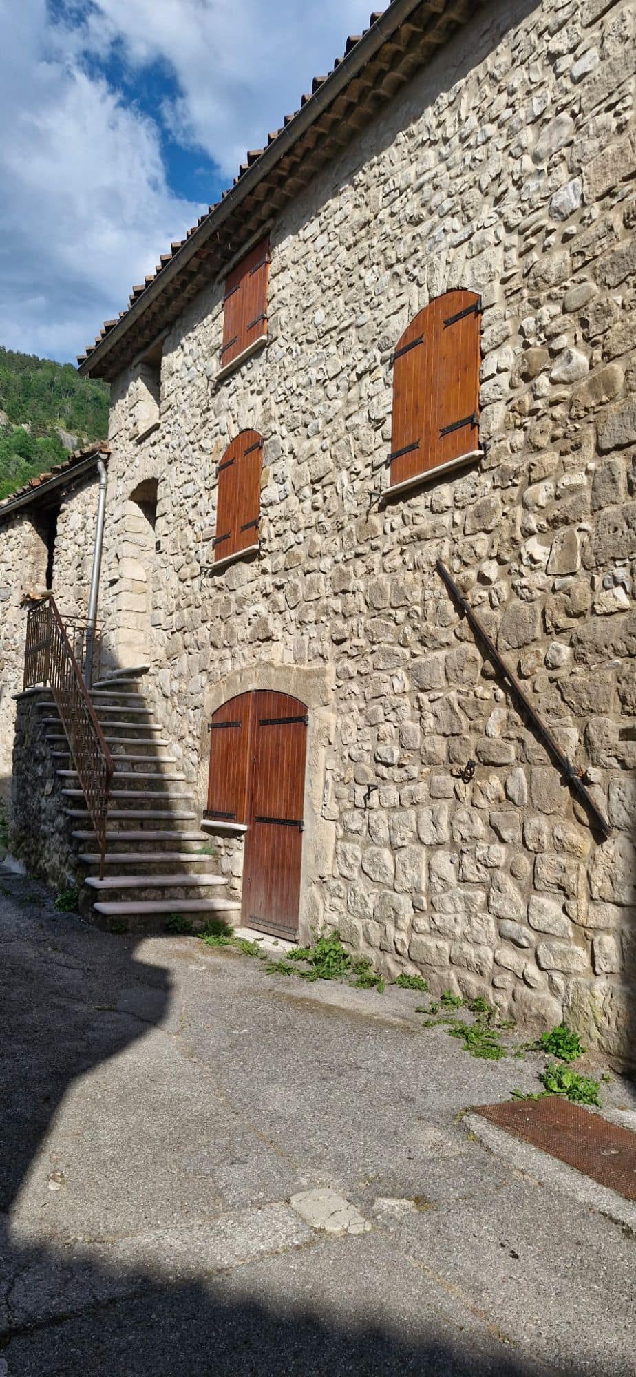 Façade de village en pierre, portes et volets cintrés, escalier extérieur maçonné.