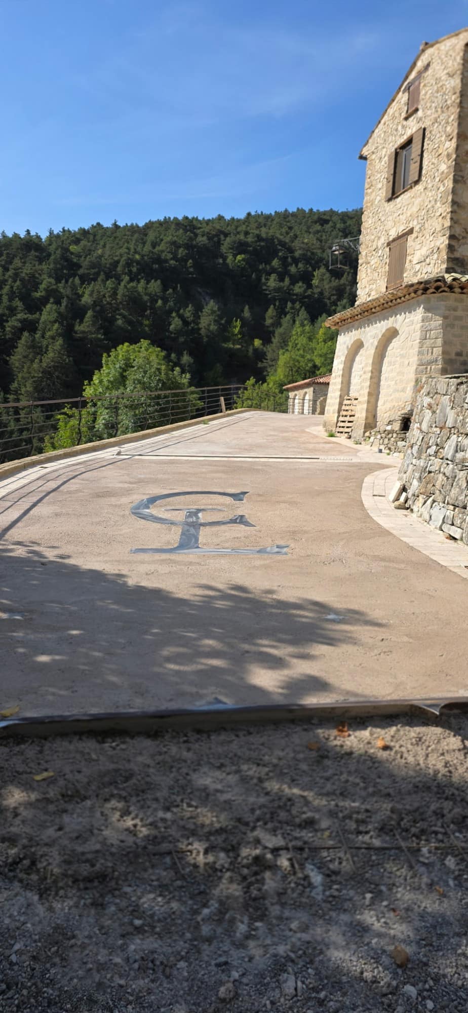 Monogramme coulé dans la dalle de la terrasse, devant la façade en pierre et ses arcs.