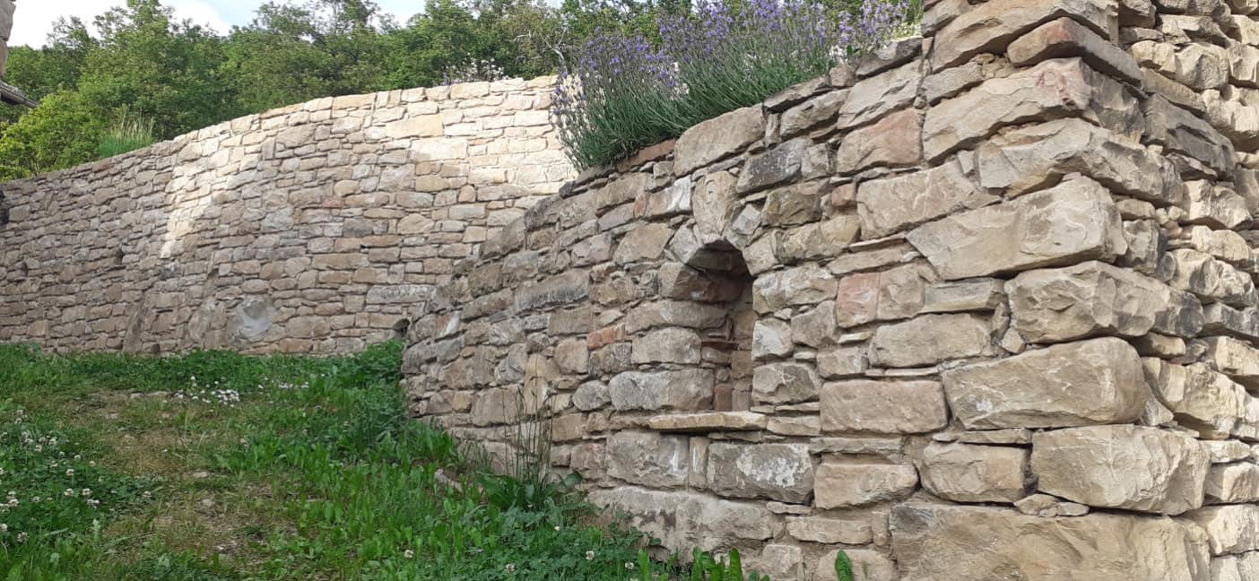 Mur en pierre sèche percé d'une niche en plein cintre, lavande en couronnement.