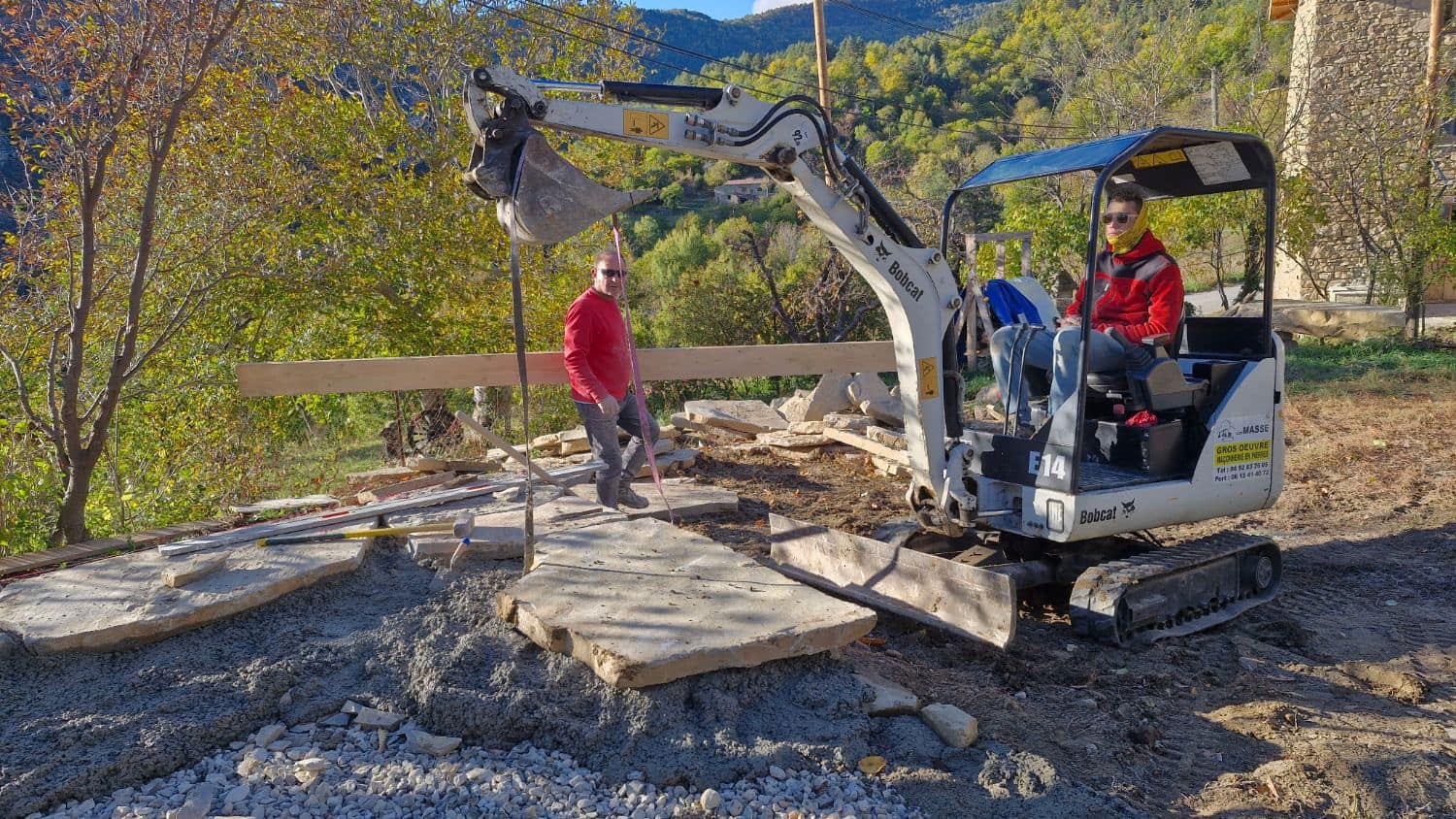 Pose de grandes dalles de pierre à la mini-pelle, deux maçons de la SARL MASSE sur le chantier.