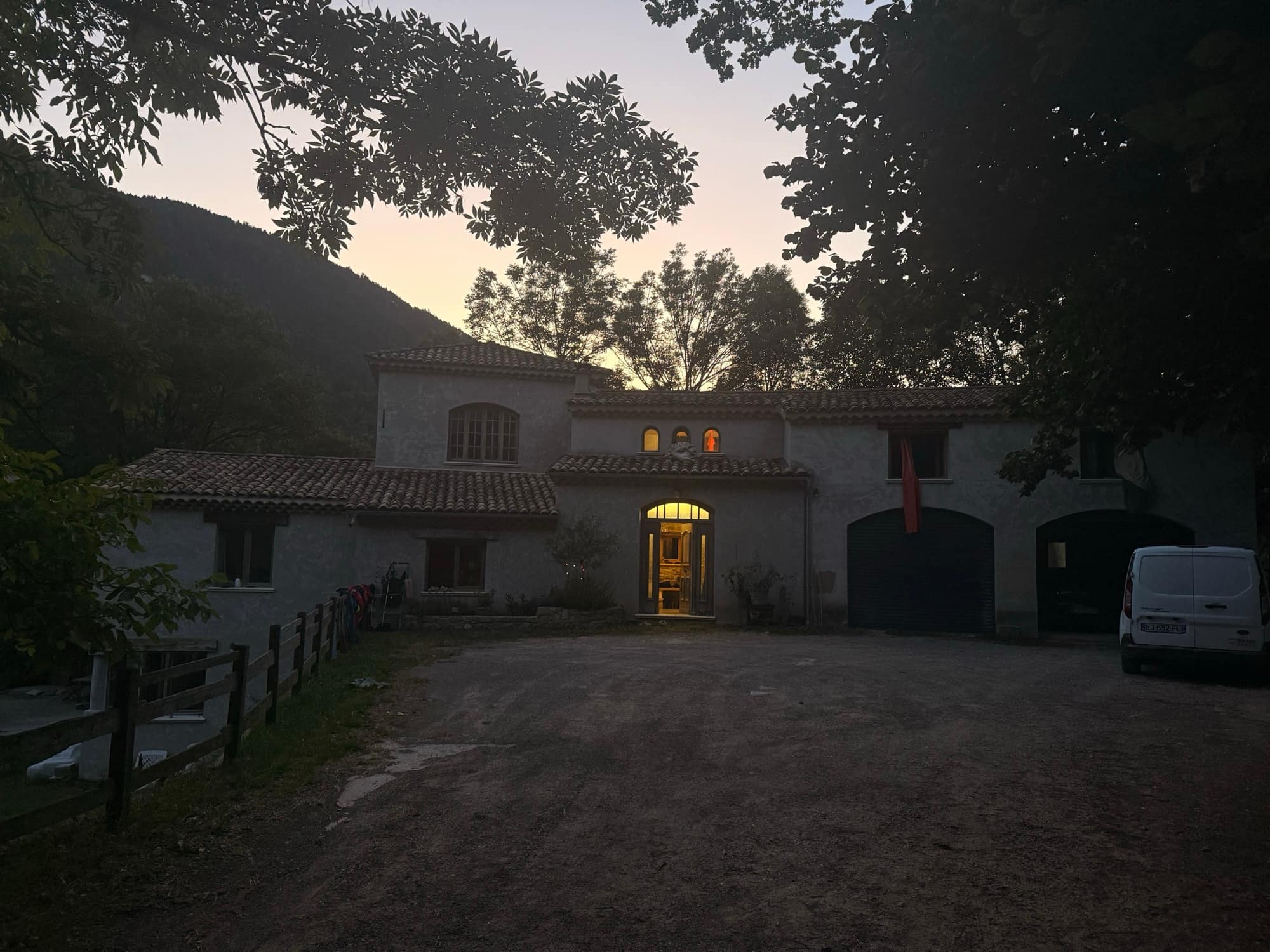 Villa en pierre construite par la SARL MASSE, éclairée de l'intérieur à la tombée du jour, montagne boisée derrière.