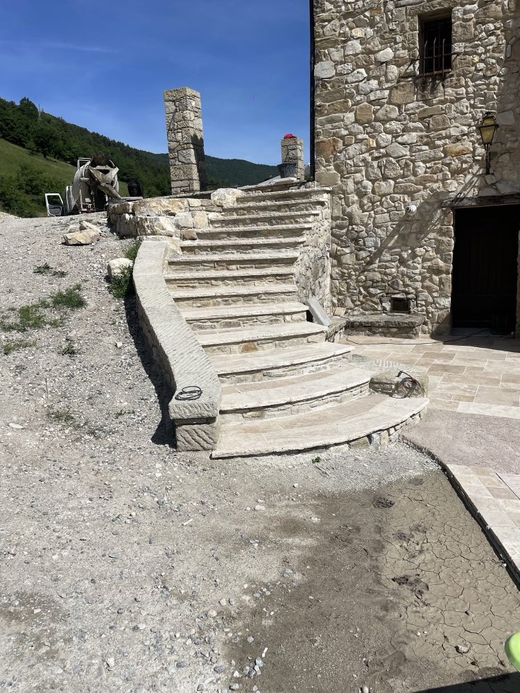 Escalier extérieur en pierre taillée, marches courbes et limon massif, contre une façade en pierre apparente.